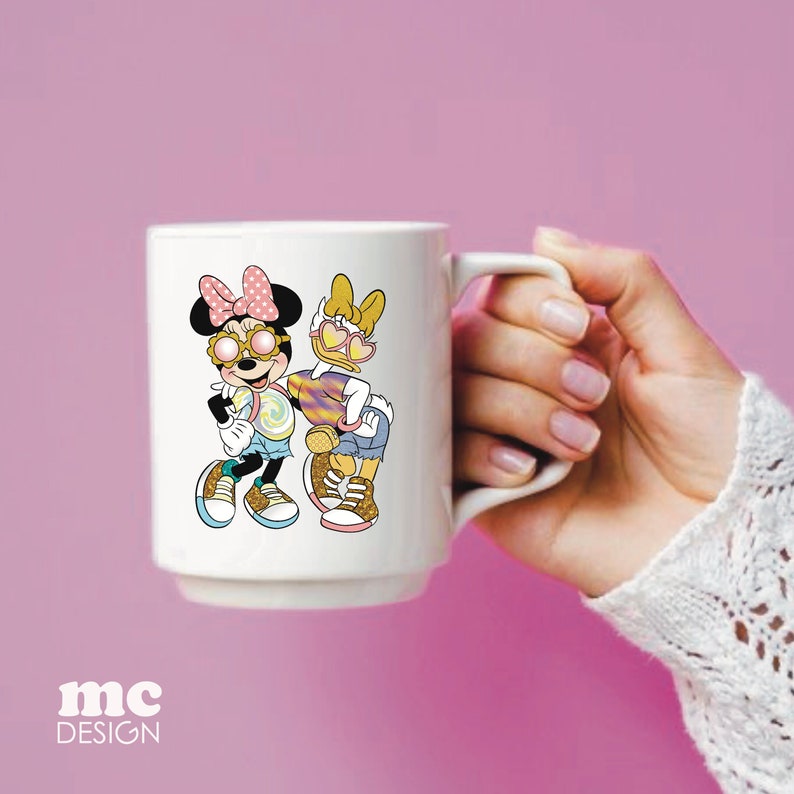 Op de afbeelding: Een witte keramische mok met een kleurrijke illustratie van twee cartoonfiguren die een zonnebril dragen. De personages zijn een muis met roze oren en een eend met gele veren. De mok heeft een zwart handvat.