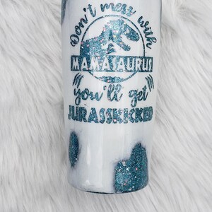 May include: White tumbler with a blue glitter design and the text "Don't mess with Mamaaurus you'll get Jurasskicked".
