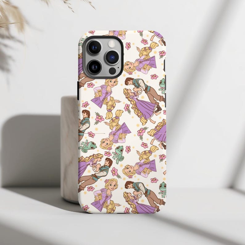May include: A white phone case with a repeating pattern of Rapunzel and Flynn Rider from the Disney movie Tangled. The pattern includes a green chameleon, flowers, and hearts. The phone case has a camera cutout and a black border.