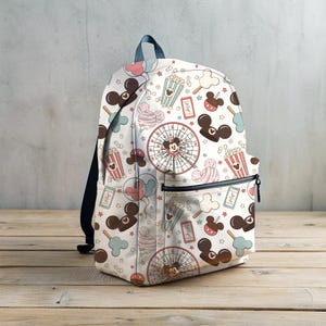 May include: White backpack with a colorful pattern of Mickey Mouse heads, popcorn buckets, balloons, and candy. The pattern is repeated all over the backpack.