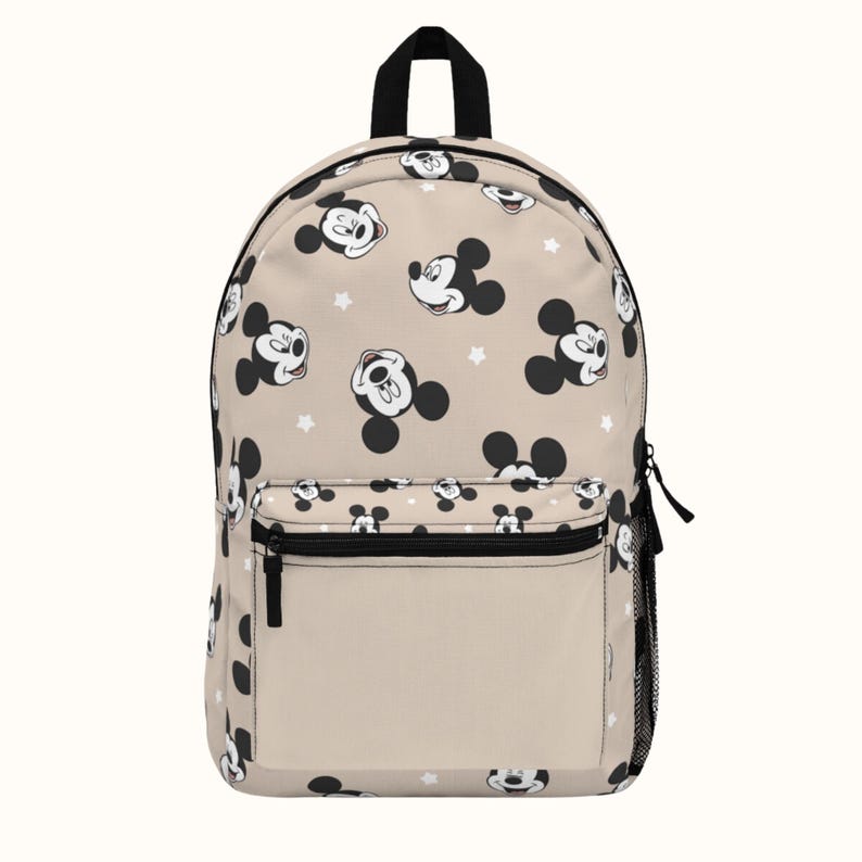 Puede incluir: Una mochila beige con un patr&oacute;n repetido de caras de Mickey Mouse y estrellas blancas. La mochila tiene una cremallera negra y un bolsillo de malla negra en el lateral.