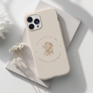 May include: A beige phone case with a rose and the text "Tale as old as time, song as old as rhyme".