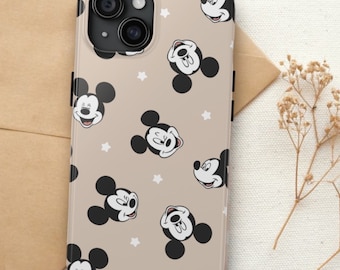 以下が含まれることがあります： ベージュ色のスマートフォンケースで、様々な表情のミッキーマウスの顔が繰り返し描かれ、小さな白い星が散りばめられています。ケースの左上隅には黒いカメラ用の切り抜きがあり、側面には黒いボタンが付いています。