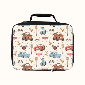 May include: A white lunch bag with a black zipper and handle. The bag features a repeating pattern of cartoon cars, traffic lights, cones, and checkered flags. The cars are red, blue, and brown.