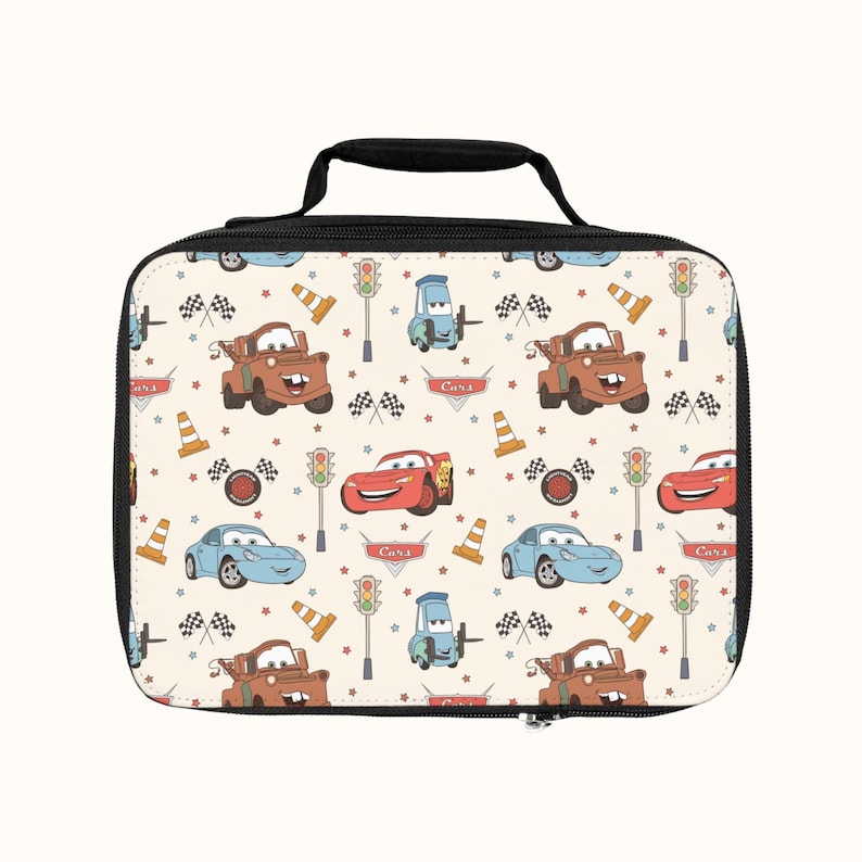 May include: A white lunch bag with a black zipper and handle. The bag features a repeating pattern of cartoon cars, traffic lights, cones, and checkered flags. The cars are red, blue, and brown.