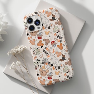 May include: A white phone case with a repeating pattern of Halloween-themed cartoon characters, pumpkins, ghosts, and the words "Spook Vibes" in orange and black. The case has a glossy finish and a camera cutout.