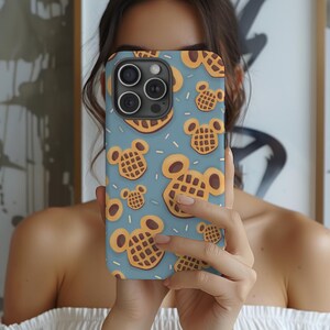 May include: A blue phone case featuring a pattern of cartoon waffles in the shape of a mouse's head. The waffles are brown with a grid pattern, and the case has a camera cutout.