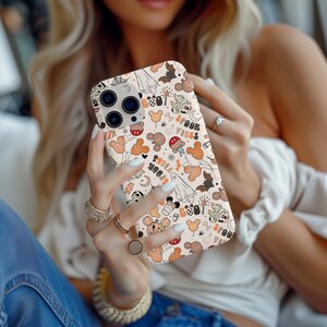 May include: A phone case with a Halloween design, featuring pumpkins, bats, ghosts, and Mickey Mouse characters in orange, black, and white. The words "Spook Vibes" are printed on the case.