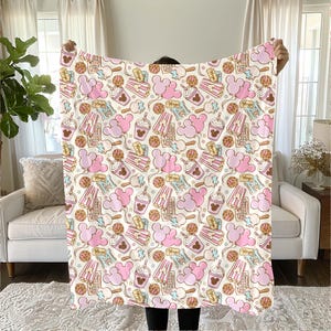 Peut inclure: Une couverture pour b&eacute;b&eacute; rose et blanche avec un motif r&eacute;p&eacute;t&eacute; d'oreilles de Mickey Mouse, de seaux de pop-corn et de cornets de glace. La couverture est faite d'un tissu doux et confortable, parfait pour se blottir.