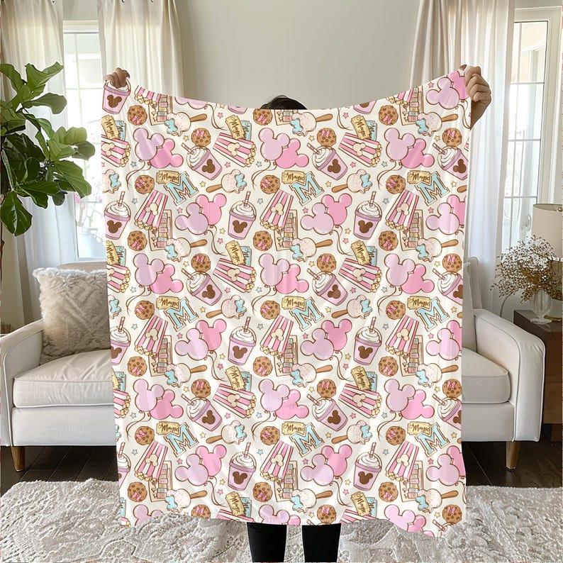 Peut inclure: Une couverture pour b&eacute;b&eacute; rose et blanche avec un motif r&eacute;p&eacute;t&eacute; d'oreilles de Mickey Mouse, de seaux de pop-corn et de cornets de glace. La couverture est faite d'un tissu doux et confortable, parfait pour se blottir.