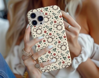 May include: A cream-colored phone case with a repeating pattern of green leaves, red stars, and floral number eight designs. The phone case has a camera cutout and is held by a person.
