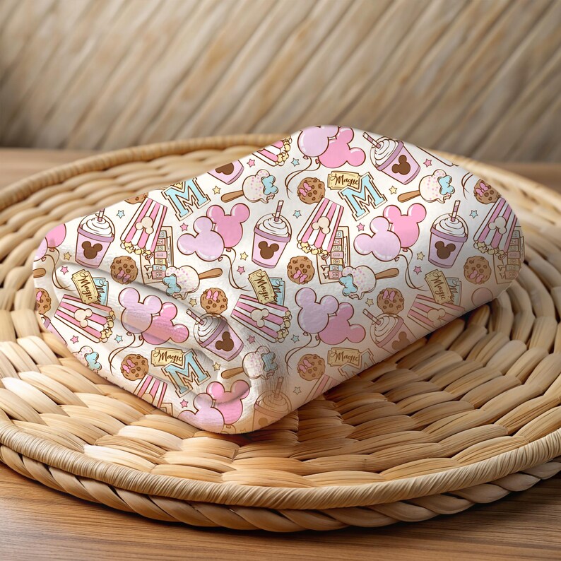 Peut inclure: Un tissu blanc avec un motif rose et bleu de t&ecirc;tes de Mickey Mouse, des seaux de pop-corn, des cornets de glace et le mot "Magic".