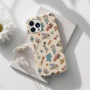 May include: A cream-colored phone case with a repeating pattern of cartoon characters from popular animated films. The case features characters like Buzz Lightyear, Woody, and the Incredibles.