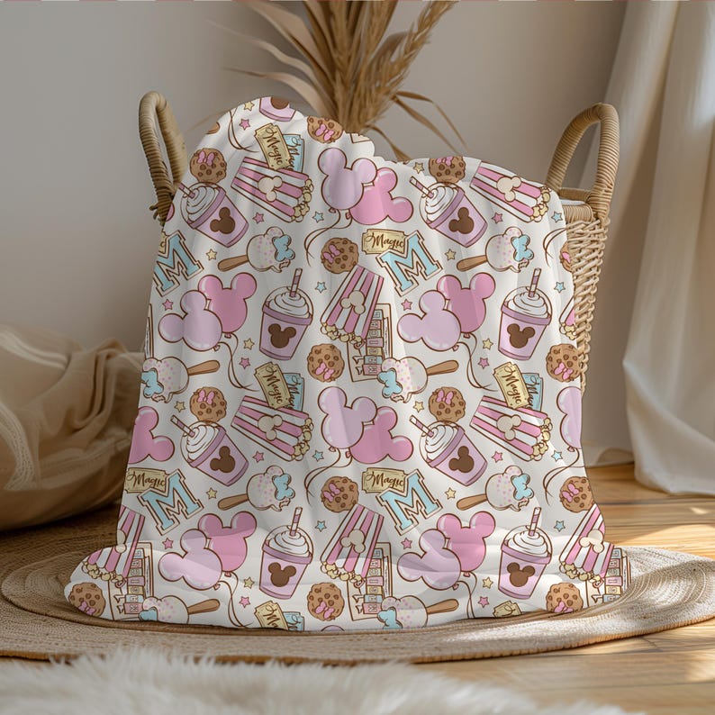 Peut inclure: Une couverture pour b&eacute;b&eacute; rose et blanche sur le th&egrave;me de Mickey Mouse. La couverture pr&eacute;sente des oreilles de Mickey Mouse, des seaux de pop-corn et des boissons. Le texte "Magic" est r&eacute;p&eacute;t&eacute; sur toute la couverture.