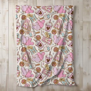 Peut inclure: Un tissu blanc avec un motif rose et marron d'oreilles de Mickey Mouse, de seaux de pop-corn, de coupes de cr&egrave;me glac&eacute;e Mickey Mouse et d'&eacute;toiles. Le texte "Magic" est r&eacute;p&eacute;t&eacute; dans tout le motif.