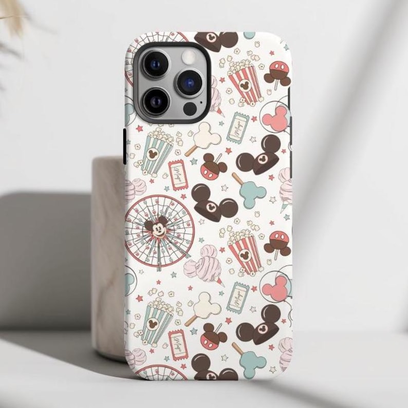 May include: A white smartphone case featuring a repeating pattern of amusement park icons including popcorn buckets, ferris wheels, balloons, tickets, and mouse-ear shaped treats in shades of brown, pink, and light blue on a white background.