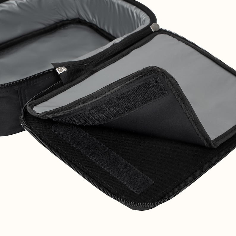 May include: Black insulated lunch bag with a zipper closure and a velcro strap. The bag is open and the inside is lined with a gray material.