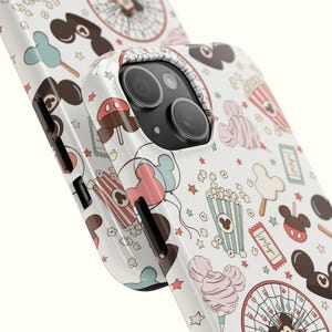 May include: A white phone case featuring a repeating pattern of carnival-themed icons including popcorn buckets, cotton candy, ferris wheels, tickets, and mouse-ear shaped treats in shades of red, blue, pink, and brown with small stars.