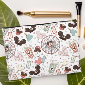 May include: White cosmetic bag with a black zip, featuring a repeating pattern of Mickey Mouse-themed carnival elements. The design includes Mickey Mouse heads, popcorn, Ferris wheels, candy floss, and balloons in pastel colours.