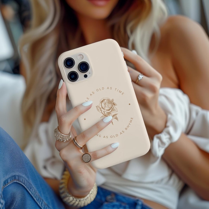 May include: A beige phone case with a gold floral design and the text "As old as time as old as rhyme".