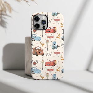 May include: A cream-colored phone case featuring a repeating pattern of characters and icons from the movie Cars, including red race cars, blue cars, brown tow trucks, traffic lights, orange traffic cones, and checkered flags.