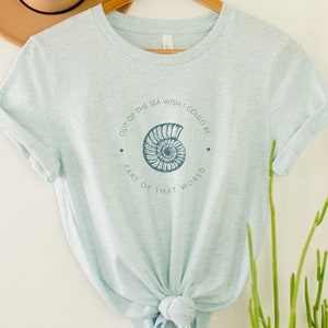 May include: A light blue t-shirt with a seashell graphic and the text "Out of the sea wish I could be part of that world".