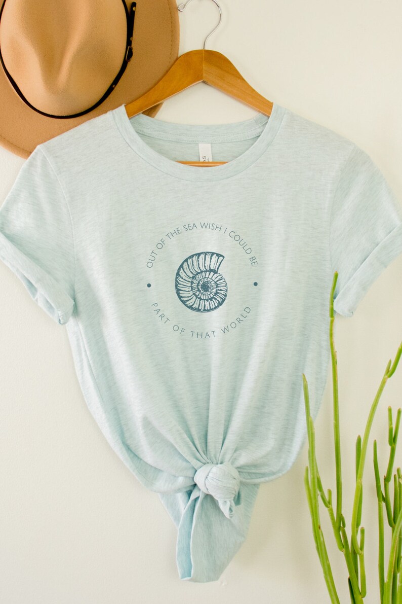 May include: A light blue t-shirt with a seashell graphic and the text "Out of the sea wish I could be part of that world".