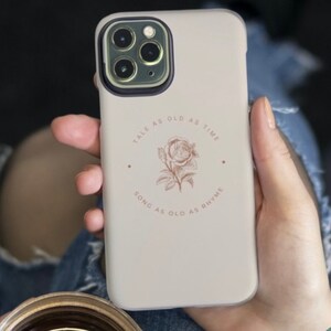 May include: A white phone case with a rose illustration and the text "Tale as old as time, song as old as rhyme".