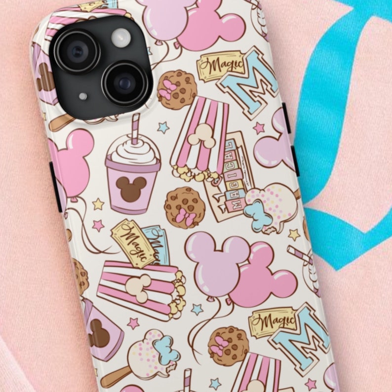 May include: A phone case with a cream background featuring a repeating pattern of pink balloons, popcorn buckets, chocolate chip cookies, ice cream bars, and tickets labeled Magic. The design includes light blue letter M icons.