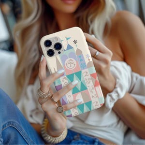 Puede incluir: Una funda blanca para iPhone con un dise&ntilde;o geom&eacute;trico colorido que presenta un castillo de dibujos animados, n&uacute;meros y una cara sonriente. La funda tiene un recorte para el objetivo de la c&aacute;mara.