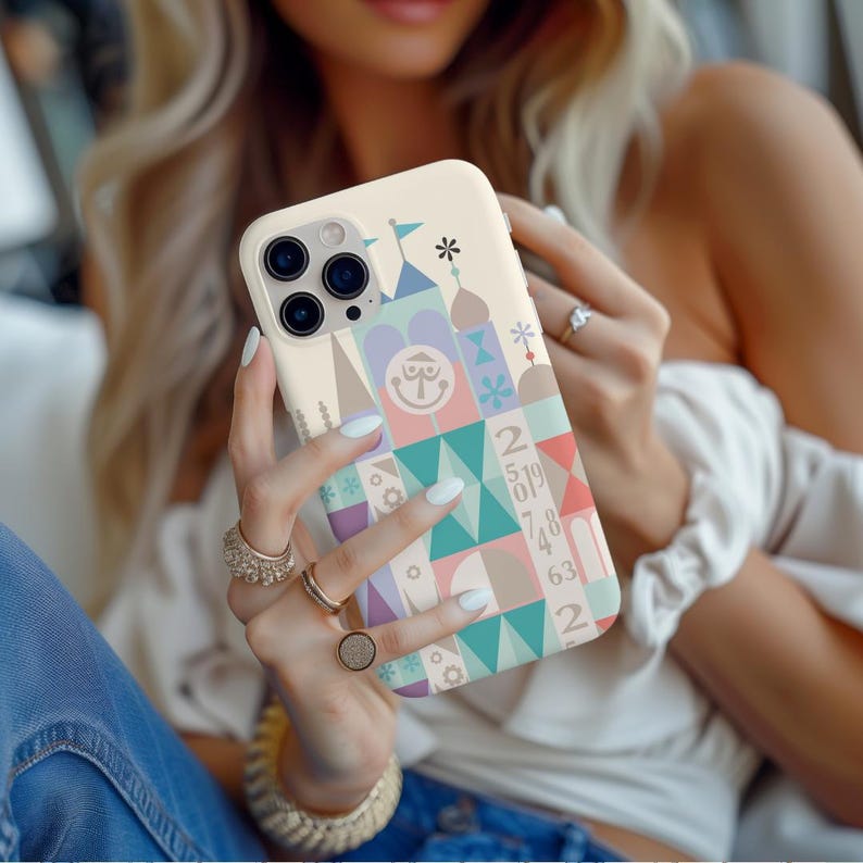 Puede incluir: Una funda blanca para iPhone con un dise&ntilde;o geom&eacute;trico colorido que presenta un castillo de dibujos animados, n&uacute;meros y una cara sonriente. La funda tiene un recorte para el objetivo de la c&aacute;mara.
