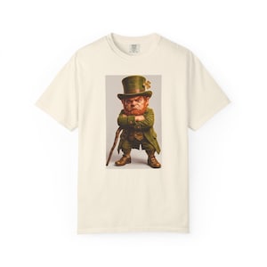 Op de afbeelding: Crèmekleurig T-shirt met een afbeelding van een leprechaun. De leprechaun heeft een rode baard, groene outfit, hoge hoed en wandelstok. De afbeelding is gecentreerd op het shirt.