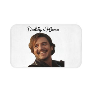 Puede incluir: Alfombra de baño blanca con la cara de un hombre sonriente y el texto "Daddy's Home" en cursiva negra.
