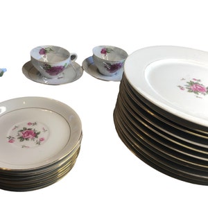 May include: A set of white porcelain dinner plates and teacups with a floral design featuring pink roses. The plates have a gold trim.