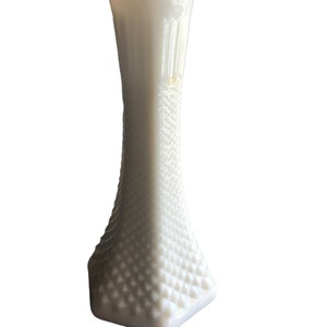 Pode incluir: Um vaso de leite branco com um padrão de diamante. O vaso é alto e fino com uma base quadrada.