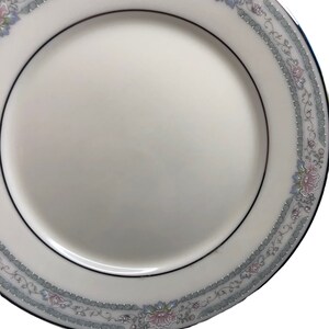 May include: A white ceramic dinner plate with a silver rim and a floral design in shades of pink, green, and blue.