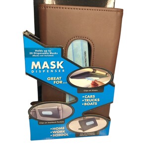 May include: A brown leather mask dispenser with a blue and white disposable mask inside. The dispenser has a flap that opens to reveal the mask. The dispenser is labeled "Mask Dispenser" and "Great For..." with a list of places to use it, including cars, trucks, boats, home, work, and school. The dispenser is also labeled "Holds up to 20 Disposable Masks (Masks not included)".