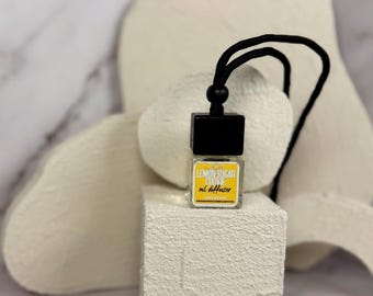 May include: A black and white car air freshener with a yellow label that reads "Lemon Sugar Cookie oil diffuser". The air freshener is hanging from a black string.
