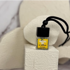 Könnte beinhalten: Ein schwarzer und gelber Auto-Lufterfrischer mit einer Schnur zum Aufhängen. Der Lufterfrischer ist mit "Pineapple Sage oil diffuser" beschriftet.