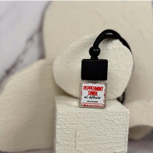 May include: A black and white car air freshener with a red and white label that says "Peppermint Swirl oil diffuser".