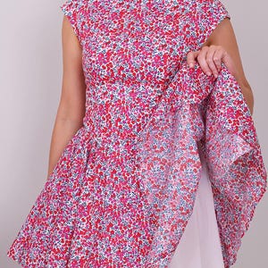 Puede incluir: Un vestido sin mangas con un estampado floral en tonos rojos y rosas sobre un fondo blanco. El vestido tiene un cuello barco y una falda acampanada. Se ve un enagua blanca debajo.