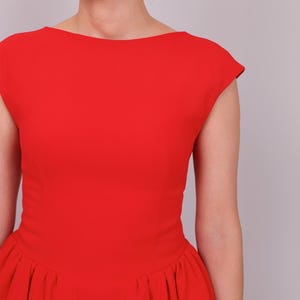 Puede incluir: Un vestido rojo vibrante con cuello barco y mangas cortas. El vestido presenta un corpi&ntilde;o ajustado que se ensancha en una falda plisada. El color brillante y el dise&ntilde;o cl&aacute;sico crean un look audaz y elegante.