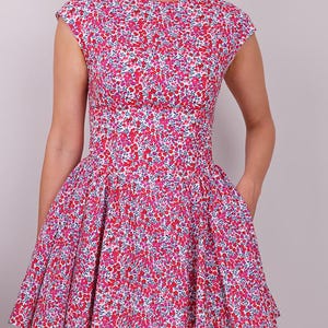 Puede incluir: Vestido sin mangas con estampado floral en tonos rosa, rojo y blanco. El vestido presenta un corpi&ntilde;o ajustado, una cintura definida y una falda acampanada. La tela est&aacute; cubierta de peque&ntilde;as flores.