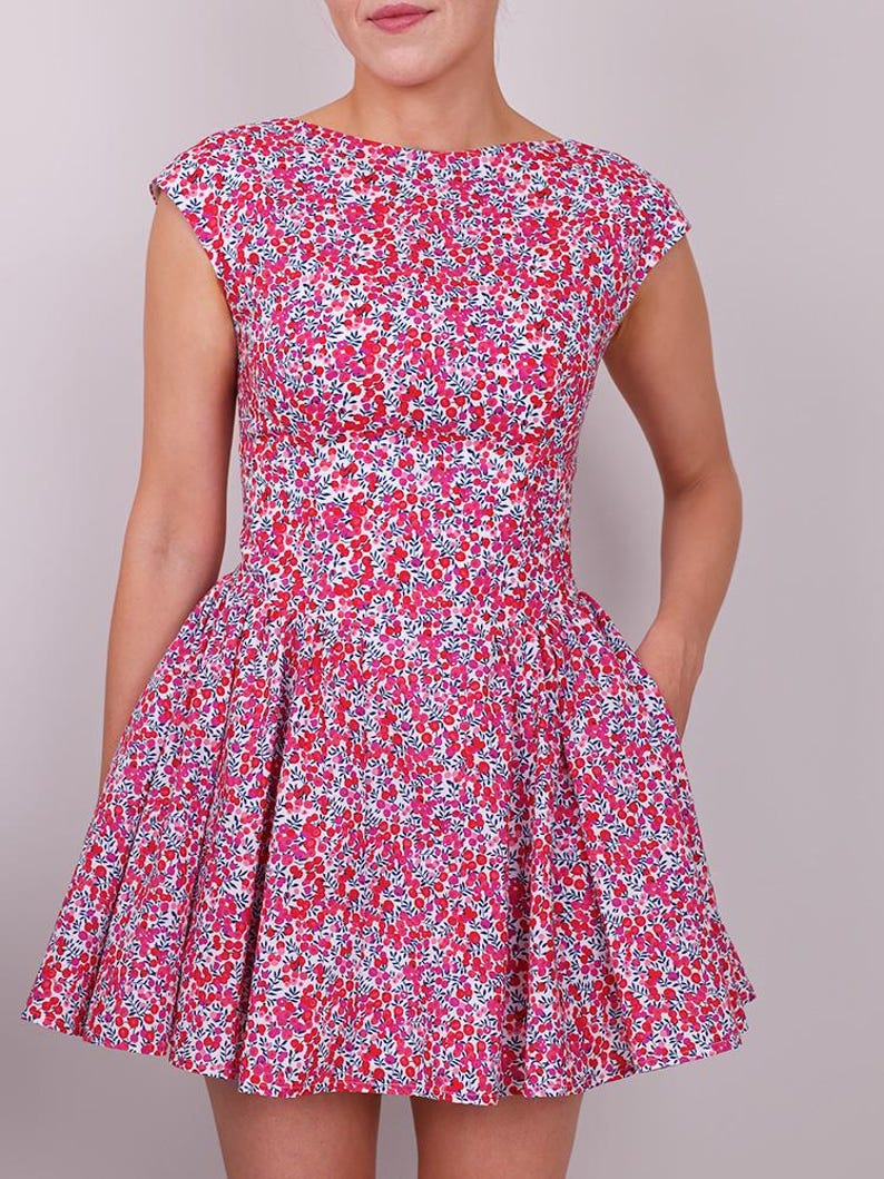 Puede incluir: Vestido sin mangas con estampado floral en tonos rosa, rojo y blanco. El vestido presenta un corpi&ntilde;o ajustado, una cintura definida y una falda acampanada. La tela est&aacute; cubierta de peque&ntilde;as flores.