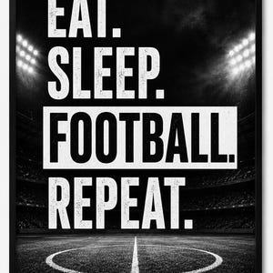 Op de afbeelding: Een zwart-wit ingelijste wanddecoratie met de tekst EAT. SLEEP. FOOTBALL. REPEAT. in dikke witte hoofdletters. De achtergrond toont een contrastrijke, korrelige foto van een voetbalstadionveld in de nacht onder felle stadionverlichting.