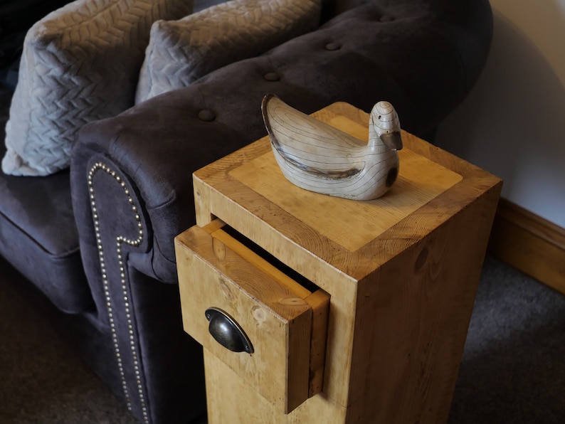 May include: A wooden side table with a drawer and a decorative duck figurine on top. The table has a light brown finish and a distressed look. The drawer has a metal handle.