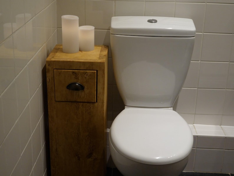 May include: A white toilet with a wooden cabinet with a drawer underneath. Two white candles are on top of the cabinet.
