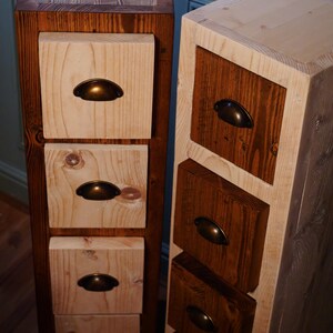Könnte beinhalten: Zwei Holzkasten mit einer hellholzfarbenen Vorderseite und einer dunkelholzfarbenen Rückseite. Jede Schublade hat einen Messinggriff.