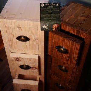 May include: Two wooden drawer units, one stained a dark brown and the other left natural. Both have four drawers with antique brass handles. The top of the natural unit has a small card with the text "Taffy & Tate Aftercare" and "Thank You".
