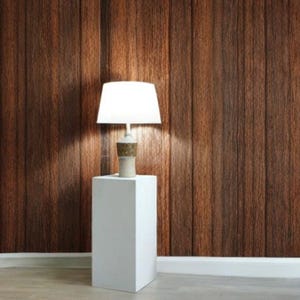 May include: A white lamp with a white shade sits on a white pedestal against a wood panel wall.